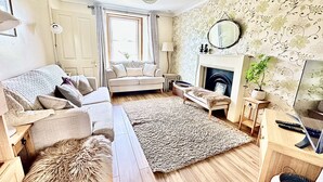 A living room with a sofa, armchair, rug, fireplace, and a mirror on the wall. - Super Pet-Friendly, Loch Front Cottage with Direct Loch Access and Games Room (Inveraray)