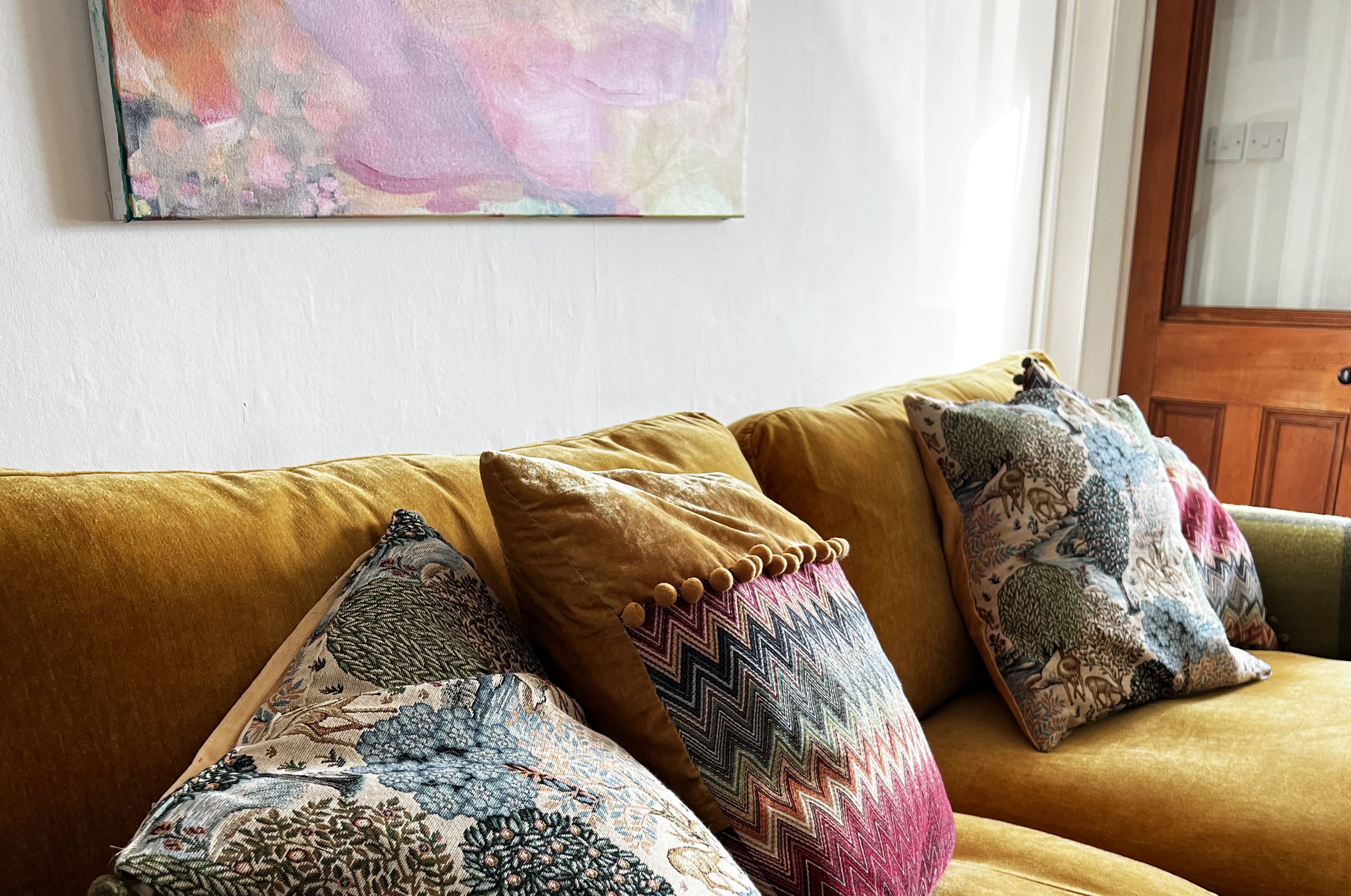A sofa with patterned cushions and a colorful abstract painting on the wall.