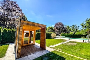 A wooden gazebo with a glass door, surrounded by a well-maintained lawn and trees.