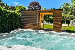 A hot tub area with a wooden structure, surrounded by a hedge and a clear sky. - Villa Austria POOL and SAUNA (Hochbruck)