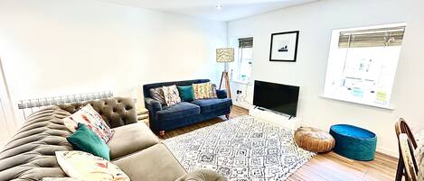 A living room with a sofa, a TV, a patterned rug, and a window with blinds.