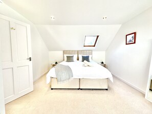Une chambre avec un grand lit, une lucarne, un tableau encadré et une porte.