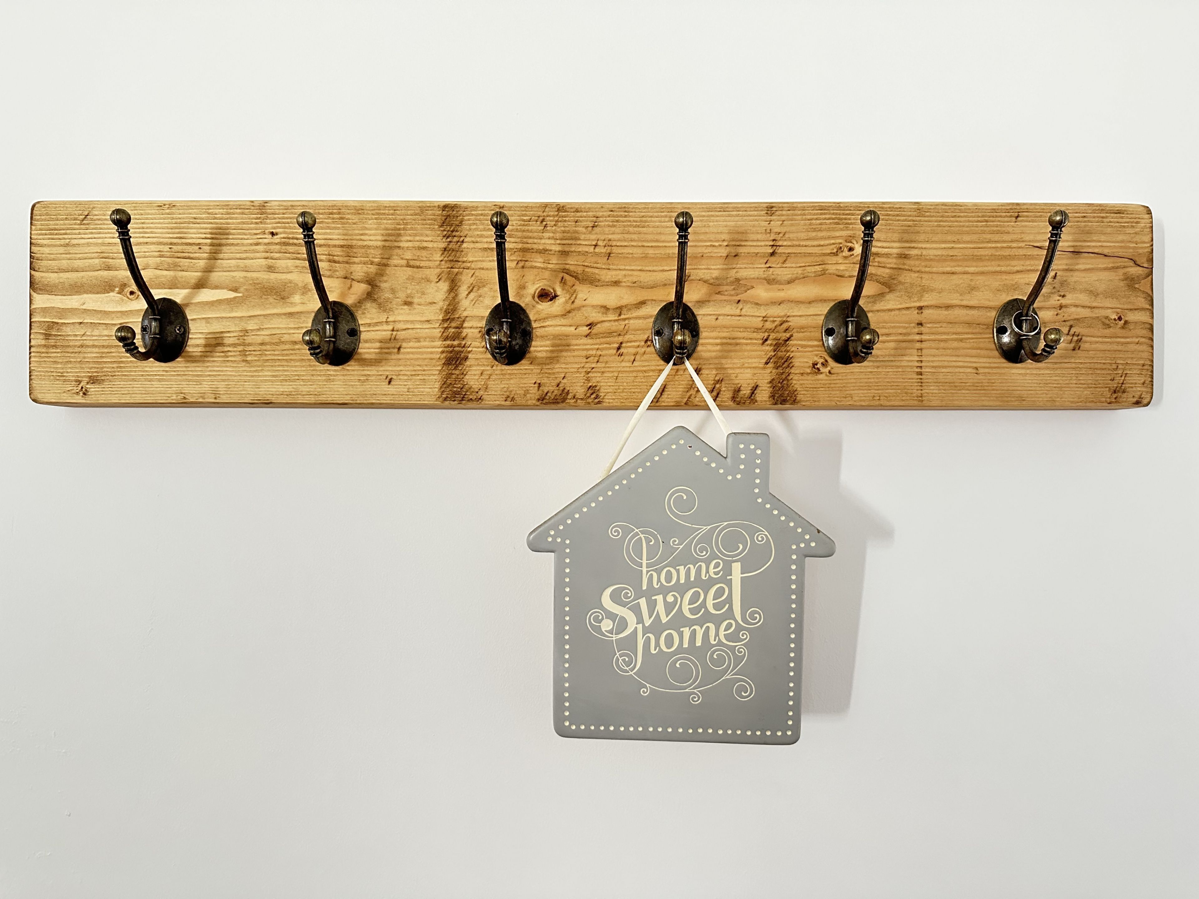 A wooden wall-mounted coat rack with five hooks and a hanging house-shaped sign below it.