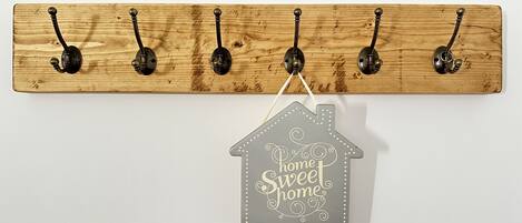 A wooden wall-mounted coat rack with five hooks and a hanging house-shaped sign below it.
