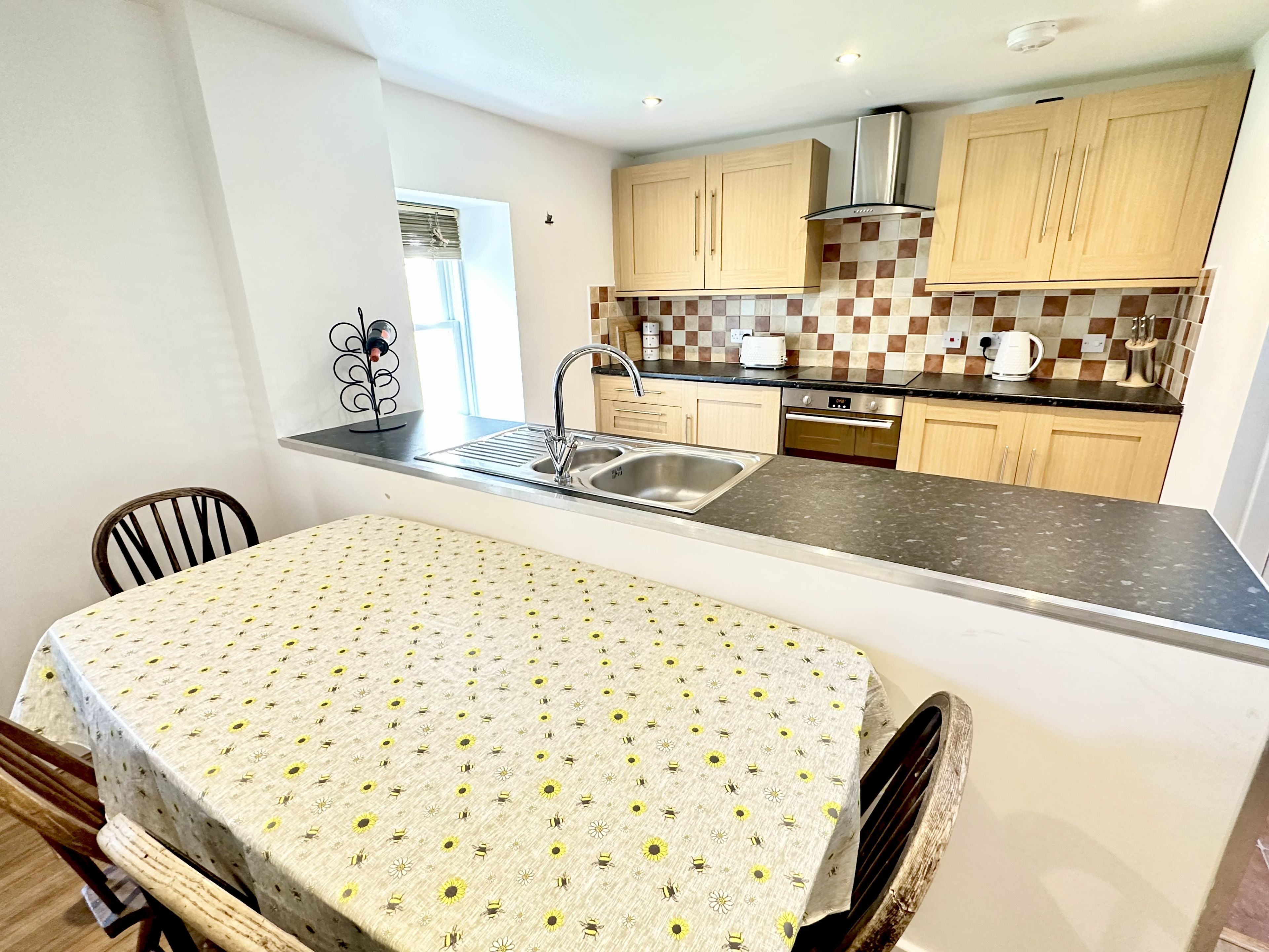 A kitchen with a central island, a dining table with a patterned tablecloth, wooden cabinets, and a stainless steel sink.