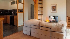 Una sala de estar moderna con un sofá, televisión y una cocina al fondo.