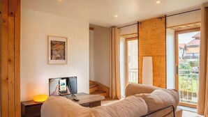 Una sala de estar moderna con un sofá, un televisor, una mesita y una ventana con cortinas.