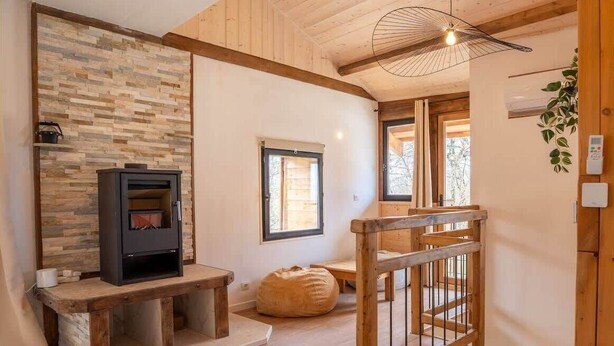 Una habitación acogedora con pared de piedra, chimenea, banco, lámpara colgante y escalera de madera.
