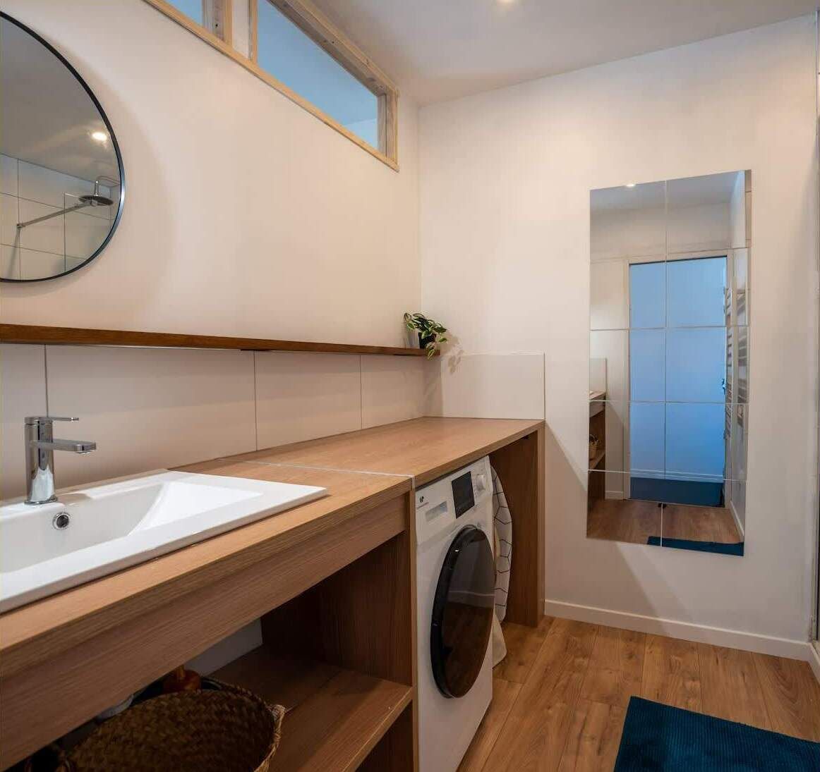 Un baño moderno con lavamanos, espejo y lavadora integrada.
