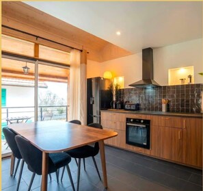 A modern kitchen with wooden cabinets, a built-in oven, and a dining area with a table and chairs.