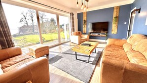 A spacious living room with leather sofas, a wooden coffee table, and a large TV. - Spacious Sleeps 10 4 Bedroom Cottage in Inveraray, Fantastic Loch Views and Big Garden (Inveraray)