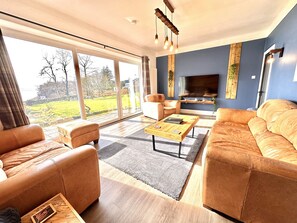 Ein geräumiges Wohnzimmer mit Ledersofas, einem Holztisch und einem großen Fernseher.