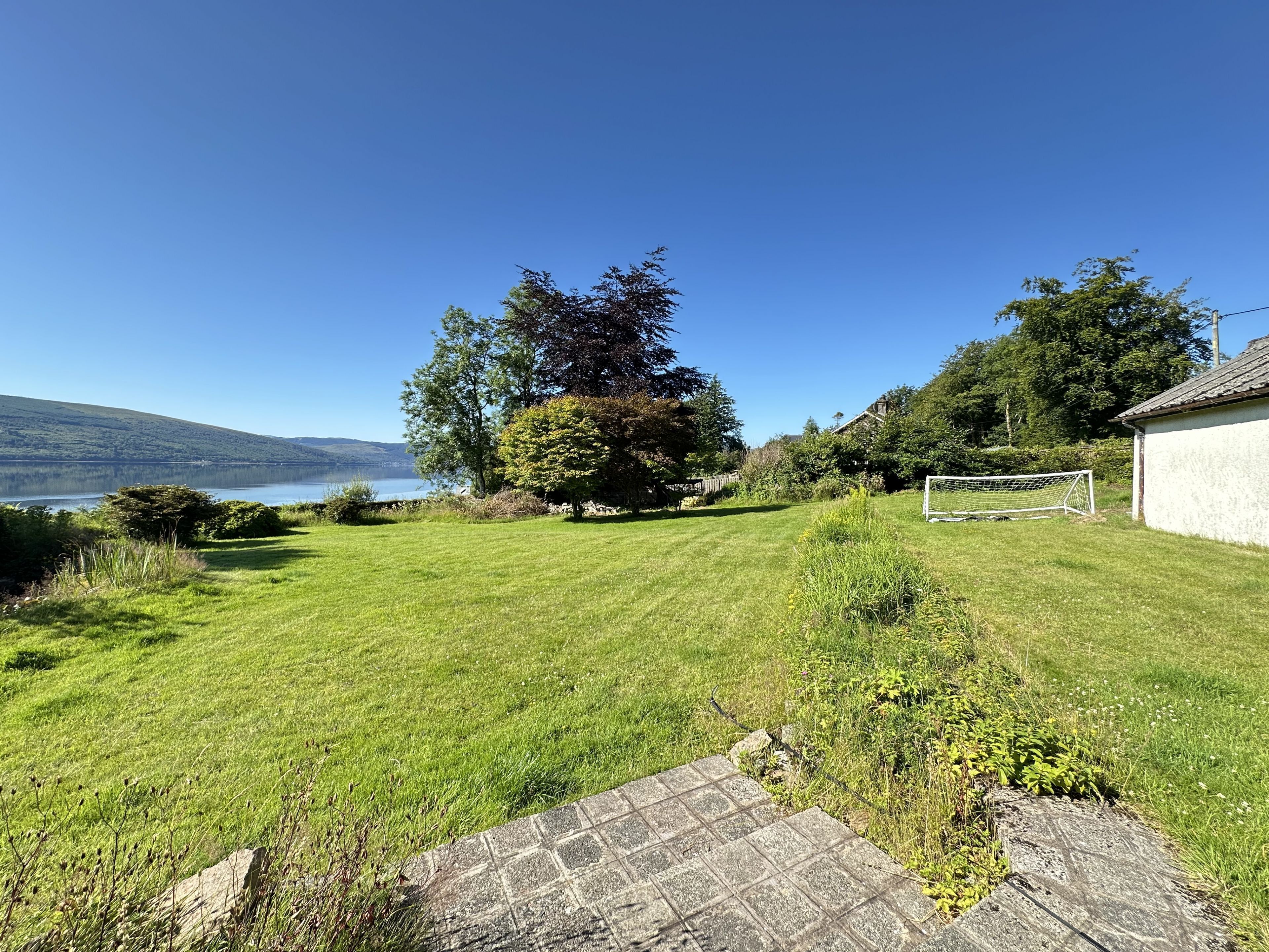 A grassy yard with a stone pathway, a white building, and a goalpost.