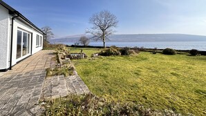 A house with a paved pathway leading to a grassy area with a view of the sea. - Spacious Sleeps 10 4 Bedroom Cottage in Inveraray, Fantastic Loch Views and Big Garden (Inveraray)