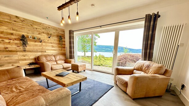 A modern living room with leather sofas, a wooden coffee table, and a large sliding glass door leading to a scenic outdoor view. - Spacious Sleeps 10 4 Bedroom Cottage in Inveraray, Fantastic Loch Views and Big Garden (Inveraray)