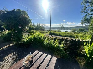 A wooden bench with a table, a bowl of cereal, and a mug. - Romantic Secluded Cosy Stone Cottage Beside the West Loch, Beautiful Argyll (Tarbert)