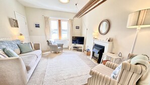 A living room with a sofa, armchair, fireplace, television, and a large window with curtains. - Romantic Secluded Cosy Stone Cottage Beside the West Loch, Beautiful Argyll (Tarbert)