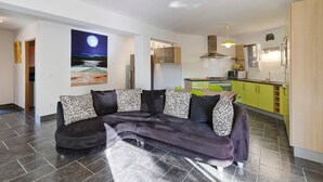 A modern living room with a dark-colored sofa, a painting of a night scene, and a kitchen area with green cabinets. - Gîte Aja Puzzuta - Sea View (Coti-Chiavari)