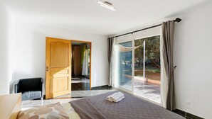 A bedroom with a bed, a chair, a wooden door, and a sliding glass door leading to an outdoor area. - Gîte Aja Puzzuta - Sea View (Coti-Chiavari)
