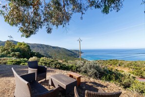 Terrassenmöbel aus Rattan, ein Holztisch und Blick auf das Meer und die Hügel.