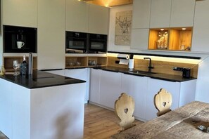 A modern kitchen with white cabinetry, a black countertop, and wooden chairs.