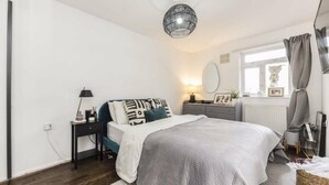A bedroom with a bed, bedside table, lamp, dresser, and a window with curtains. - Four-bedroom home in Chiswick, West London, near transport links (London)