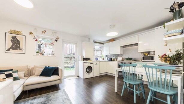 A modern kitchen with white cabinets, a dining area with blue chairs, a washing machine, and a sofa with a blue pillow. - Four-bedroom home in Chiswick, West London, near transport links (London)