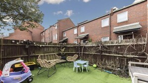 A backyard with artificial grass, a play area with a toy car, wicker chairs, and a table. - Four-bedroom home in Chiswick, West London, near transport links (London)