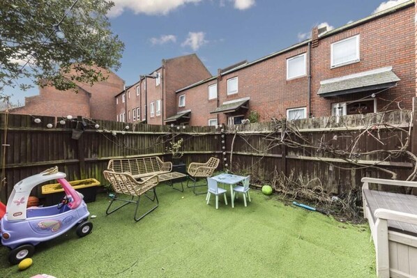 A backyard with artificial grass, a play area with a toy car, wicker chairs, and a table. - Four-bedroom home in Chiswick, West London, near transport links (London)