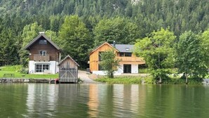 A lakeside cabin with a wooden exterior, a dock, and a forested backdrop. - SeeChalet Hallstatt (Bad Goisern am Hallstättersee)