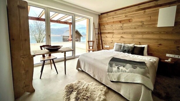A bedroom with a large bed, a wooden wall, a window, and a view of the outdoors. - SeeChalet Hallstatt (Bad Goisern am Hallstättersee)