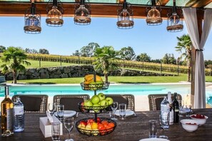 A dining table set outdoors with a pool view, fruit bowls, and wine bottles.