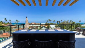 Una terraza con mesa y sillas, con vistas a la costa, palmeras y edificios.