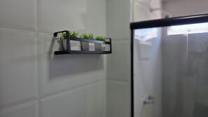 Et badeværelse med hvide fliser, en sort hylde med planter og en brusevæg i glas.