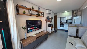 Una sala de estar moderna con un televisor de pantalla plana, estanterías de madera, un sofá y una cocina al fondo.