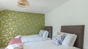 En dobbeltseng med hvid, quiltet madras og et pink tæppe, to puder, samt en vævet lampe over sengen.