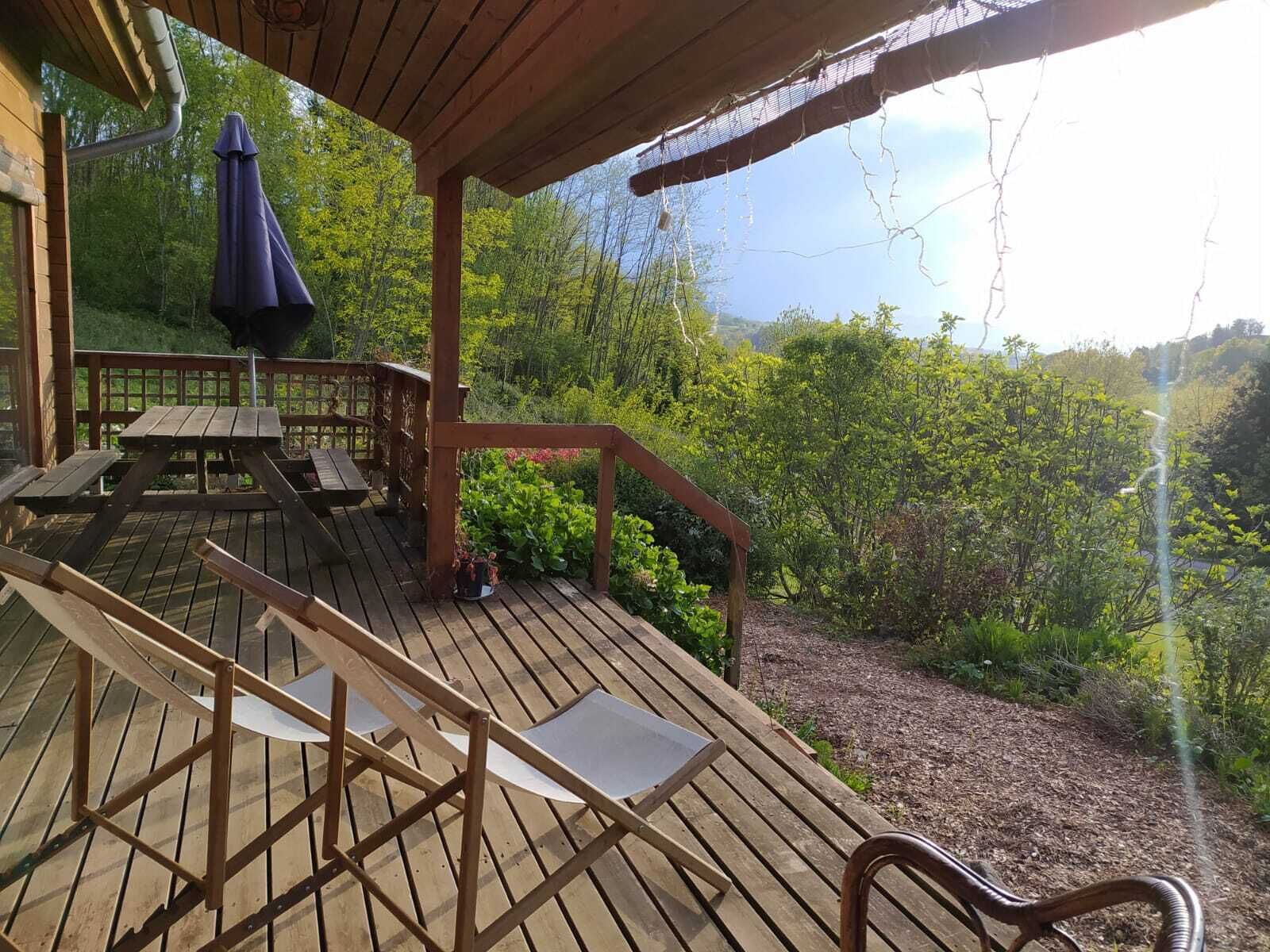 Une terrasse en bois avec des meubles d’extérieur, un espace abrité et une vue sur un paysage boisé.