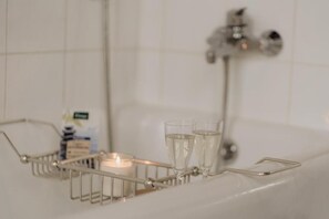 A bathroom with a bathtub, a candle, and two glasses on a tray. - B&B Kasteel Den Tip (Arendonk)