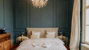 Uma cama bem arrumada com almofadas, um aparador de madeira, um candelabro e uma janela com cortinas.
