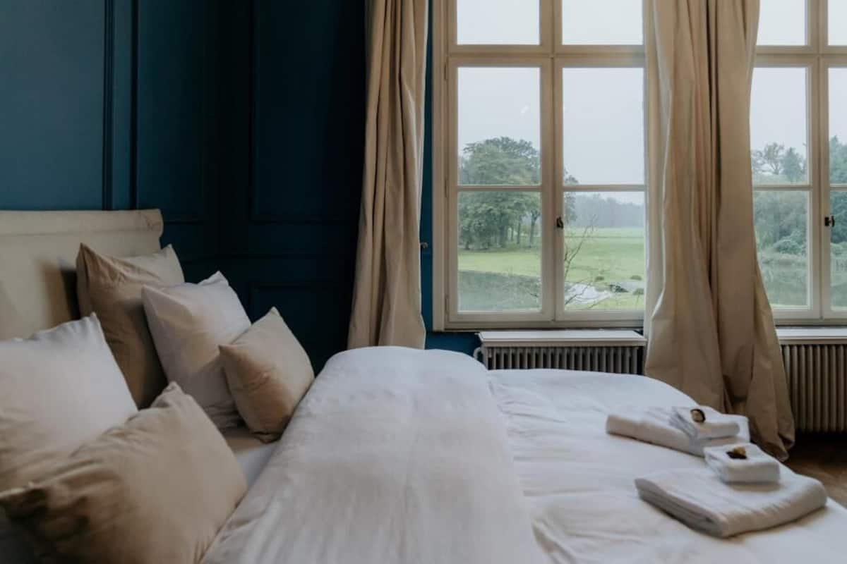 A bedroom with a bed, pillows, a window with curtains, and a view of greenery outside.