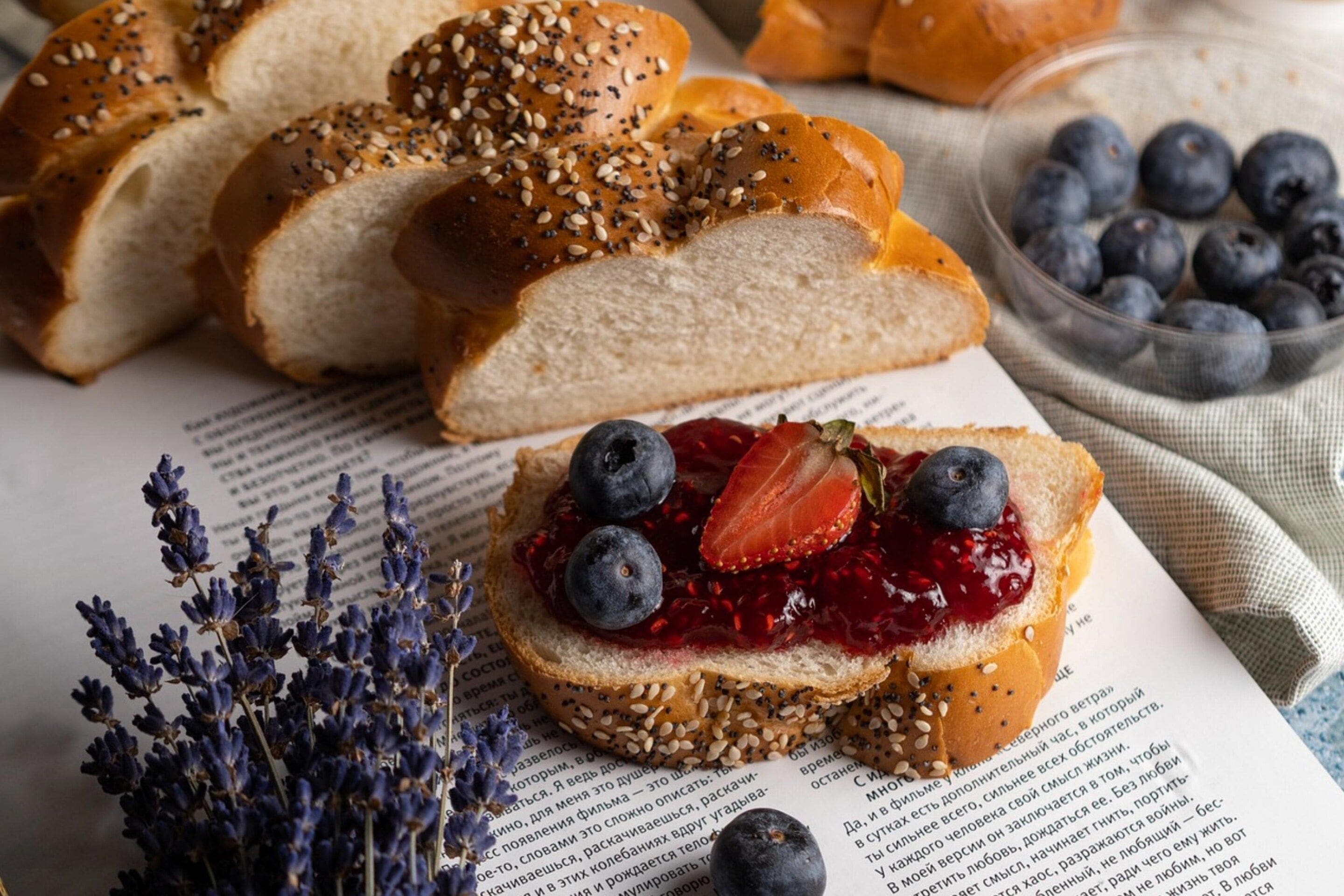 Ein Brot mit Saaten, eine Scheibe mit Marmelade und Beeren, und eine Schüssel mit Blaubeeren.