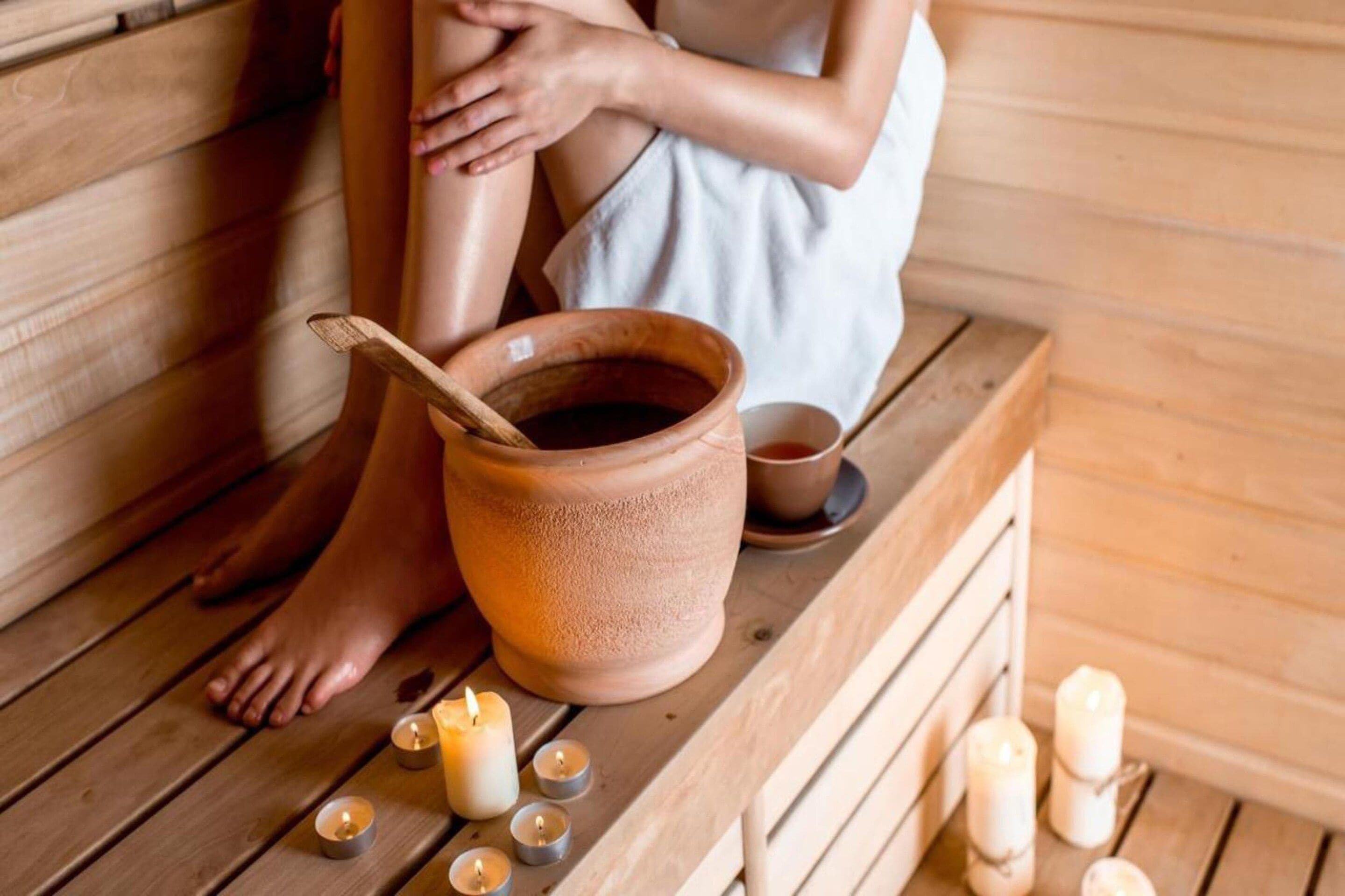 A wooden bench with a person sitting, a clay pot, and several lit candles.