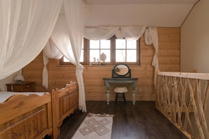 A wooden cabin bedroom with a bed, a small table, a chair, a window with curtains, and a mirror. - Comfortable Apartment With Terrace, Close to Beach (gmina Będzino)