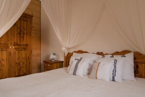 Quarto com cabeceira de madeira, cama com roupa de cama branca e mesa de cabeceira com um objeto decorativo.
