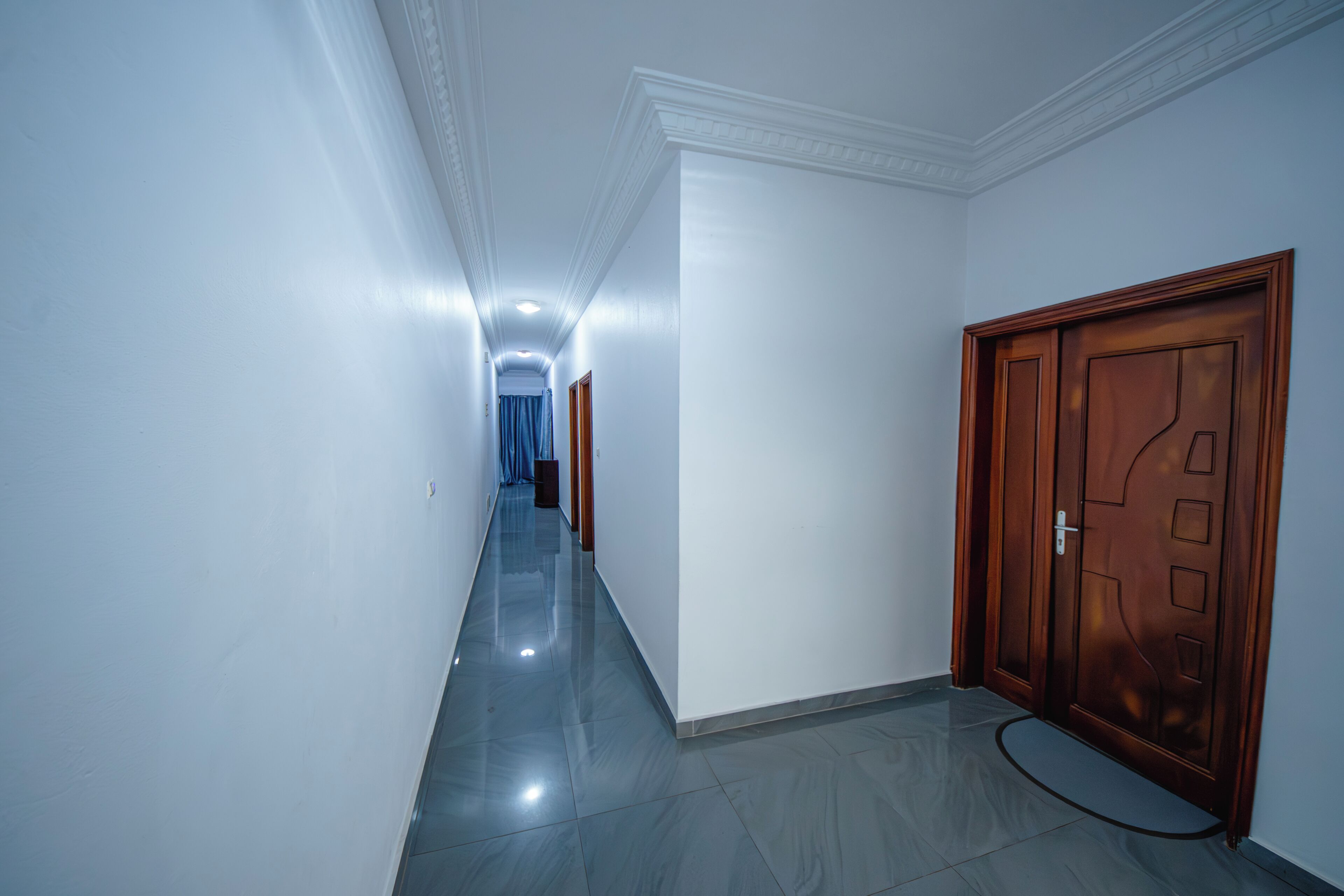 A hallway with a wooden door, white walls, and a tiled floor.