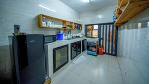 Cocina equipada con refrigerador, microondas, estufa y estantes con diversos artículos.