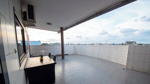 Een balkon met een betegelde vloer, een kleine tafel met een vaas en uitzicht op de stad.
