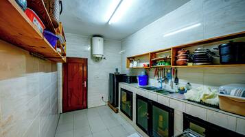 A compact kitchen with white tiled walls, a wooden door, and shelves holding kitchenware.