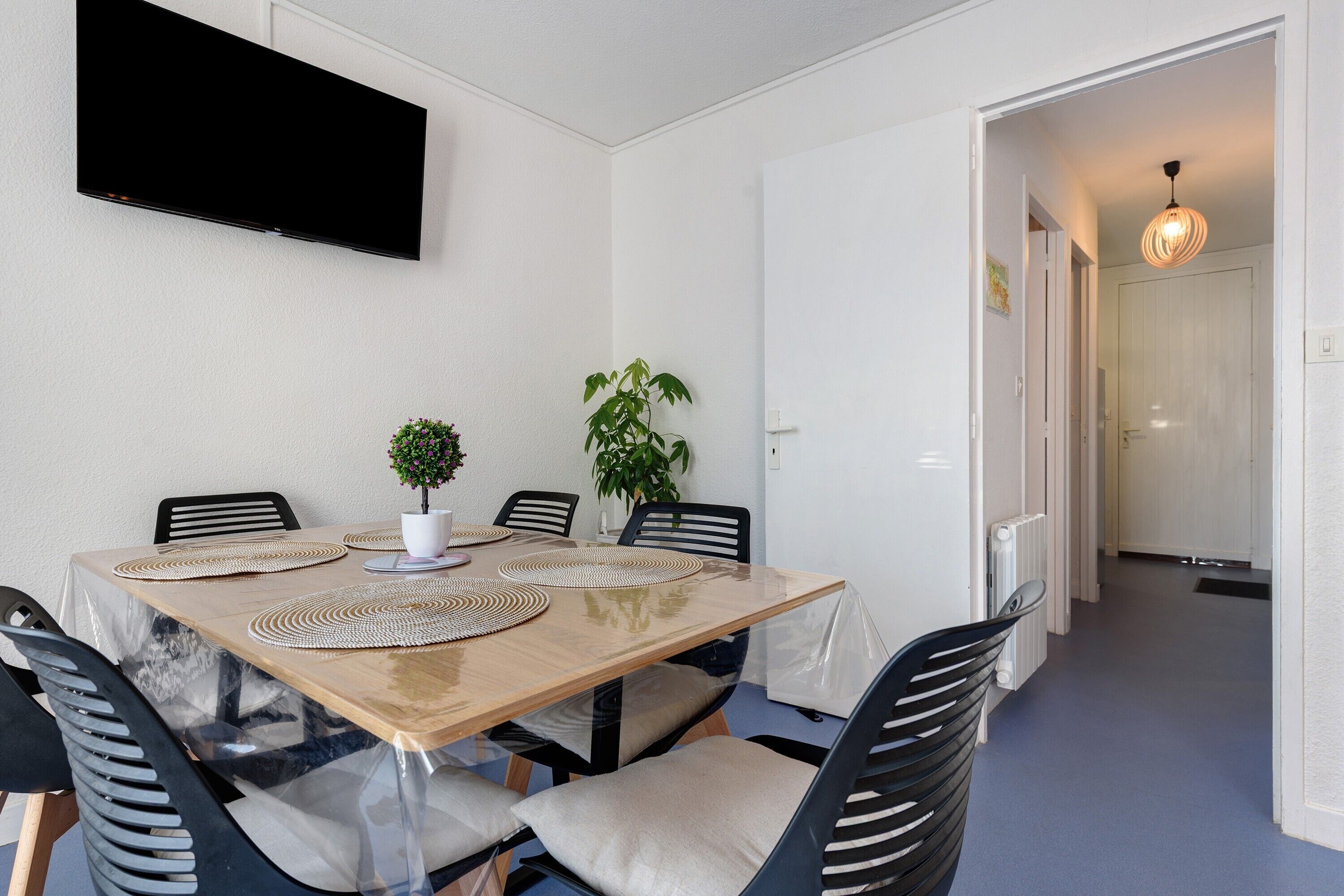 A dining area with a table, chairs, a television, and a potted plant.