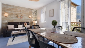 Un salón moderno con una mesa de comedor, sillas negras, un sofá y un ventanal con vistas a montañas.